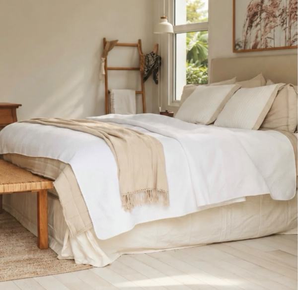 Dormitorio luminoso con ropa de cama en tonos crema y banco de madera